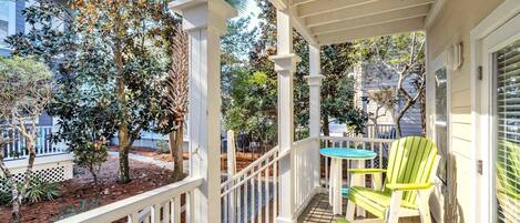 A covered porch with a wooden deck, white railings, and two green Adirondack chairs.