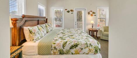 A bedroom with a large bed, a ceiling fan, and two windows with decorative shutters.