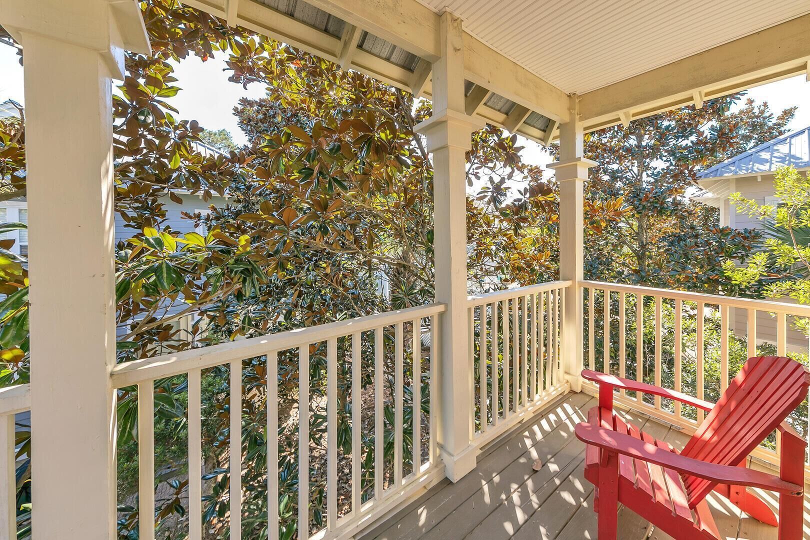 A covered porch with a red chair, white railings, and trees with autumn leaves.