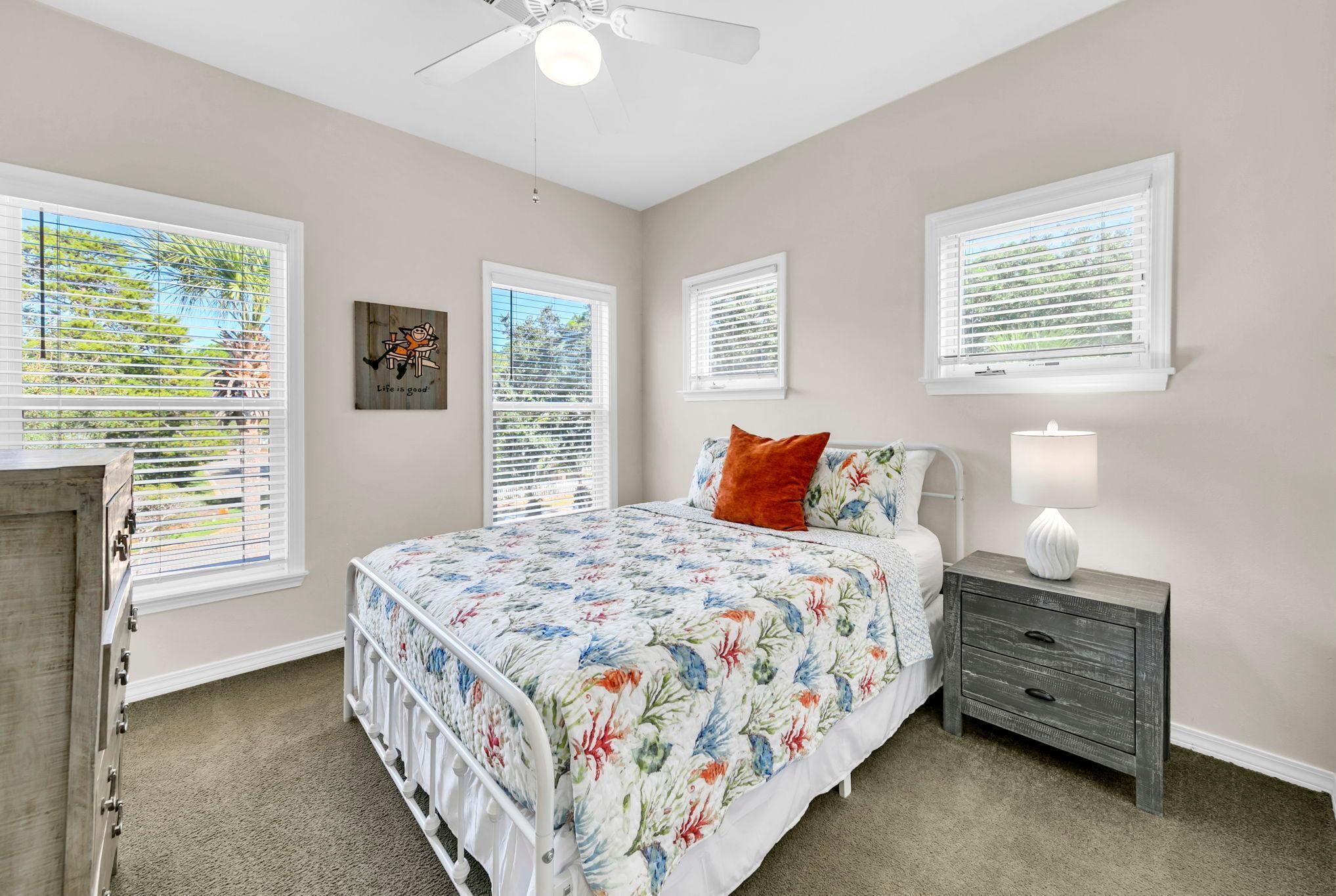 Une chambre à coucher comprenant un lit, une table de chevet, une commode et des fenêtres équipées de stores.