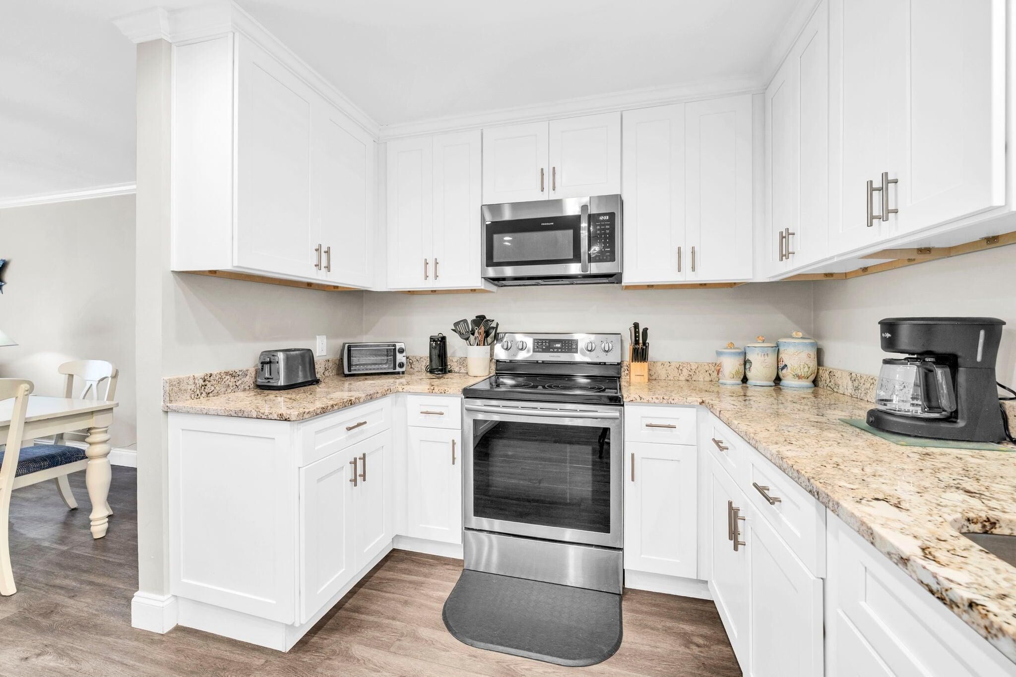 A modern kitchen with white cabinets, a stainless steel oven, a microwave, and a coffee maker.