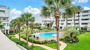 A pool surrounded by palm trees and a white building with balconies. - Aegean 213 (Destin)