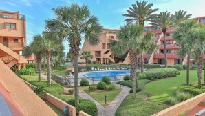 A pool area surrounded by palm trees and a building with a red roof. - Aegean 213 (Destin)