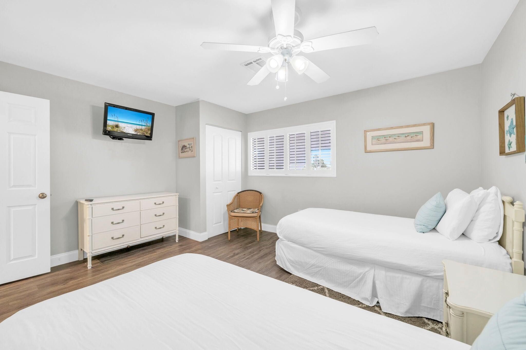 A bedroom with two beds, a ceiling fan, a TV, a dresser, a chair, and a window with blinds.