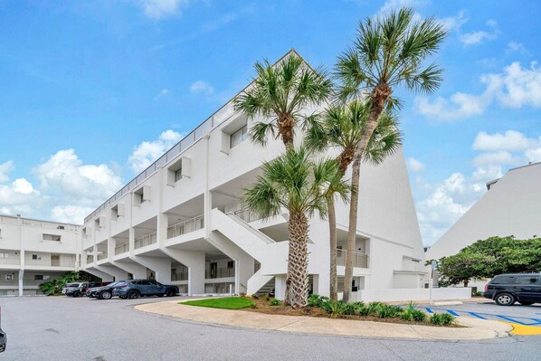 A modern multi-story building with a unique architectural design, featuring balconies and a central courtyard with palm trees. - Aegean 213 (Destin)