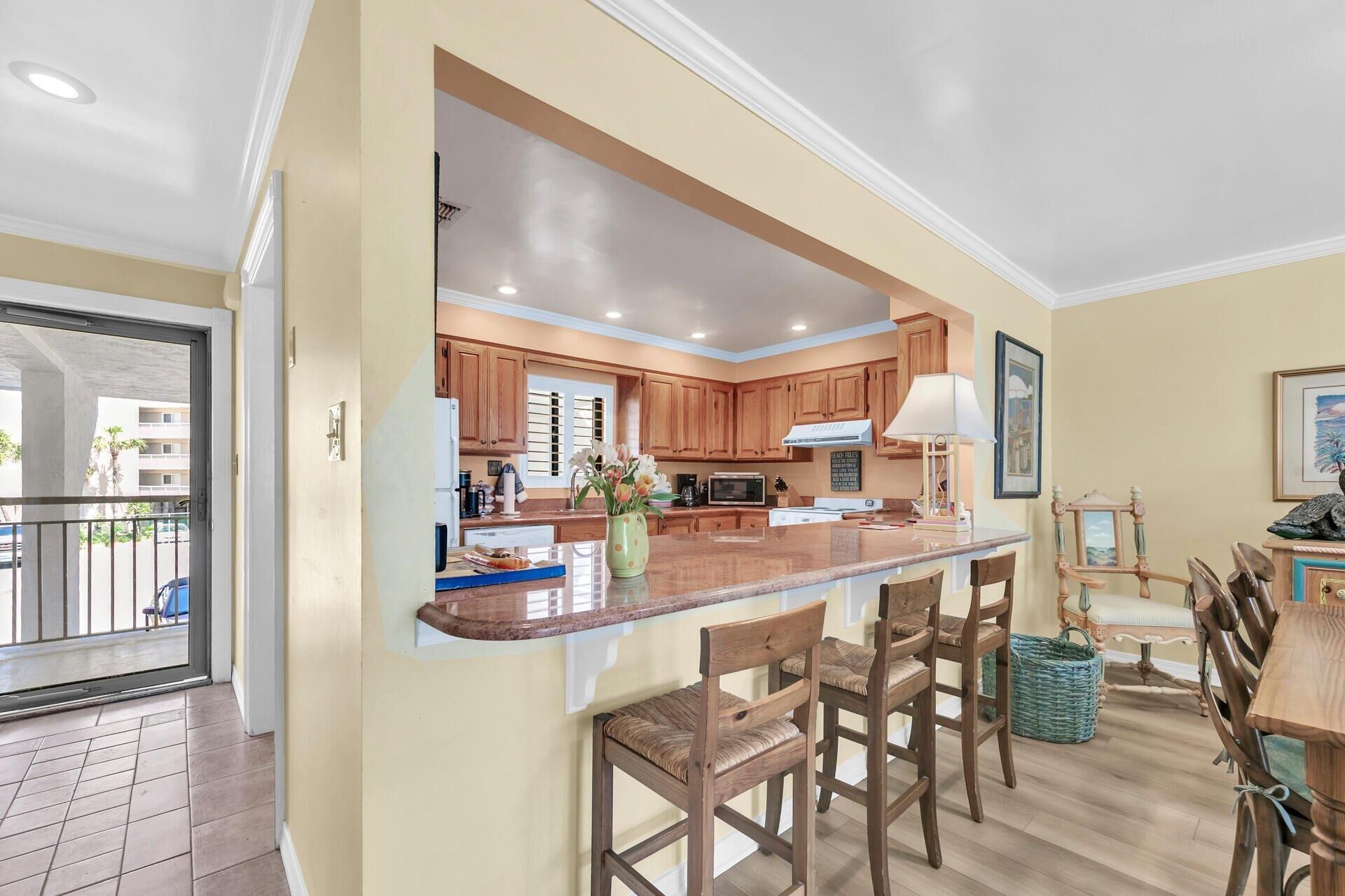 A kitchen with wooden cabinets, a central island with bar stools, and a dining area with a table and chairs.