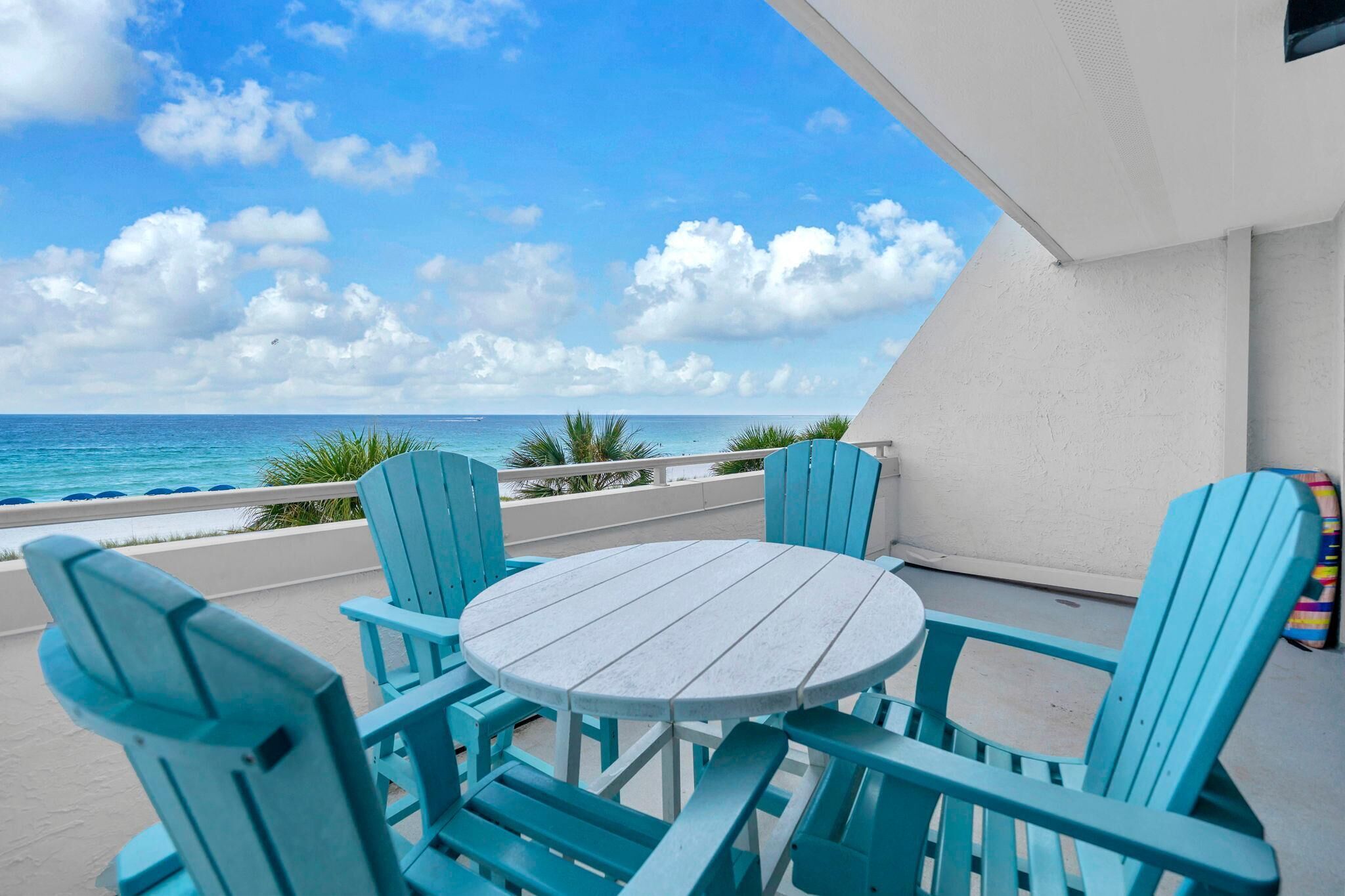 A balcony with a round table and four chairs, overlooking a beach and ocean.