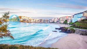 Paisagem costeira com praia, edifícios e uma linha costeira rochosa.