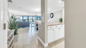 A modern kitchen with white cabinetry, a clock on the wall, and a view of the ocean through large windows. - Aegean 309 (Destin)