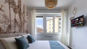 Un dormitorio con cama, un mural, televisor y ventana con cortinas.