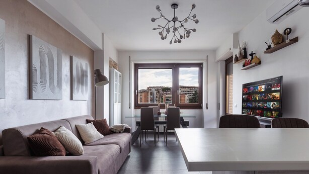 Una sala de estar moderna con un sofá, una mesa de comedor y sillas. Hay un ventanal con vistas a edificios.