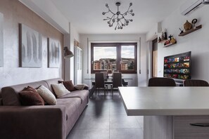 Ein modernes Wohnzimmer mit Sofa, Esstisch und Stühlen. Ein großes Fenster bietet Blick auf Gebäude.