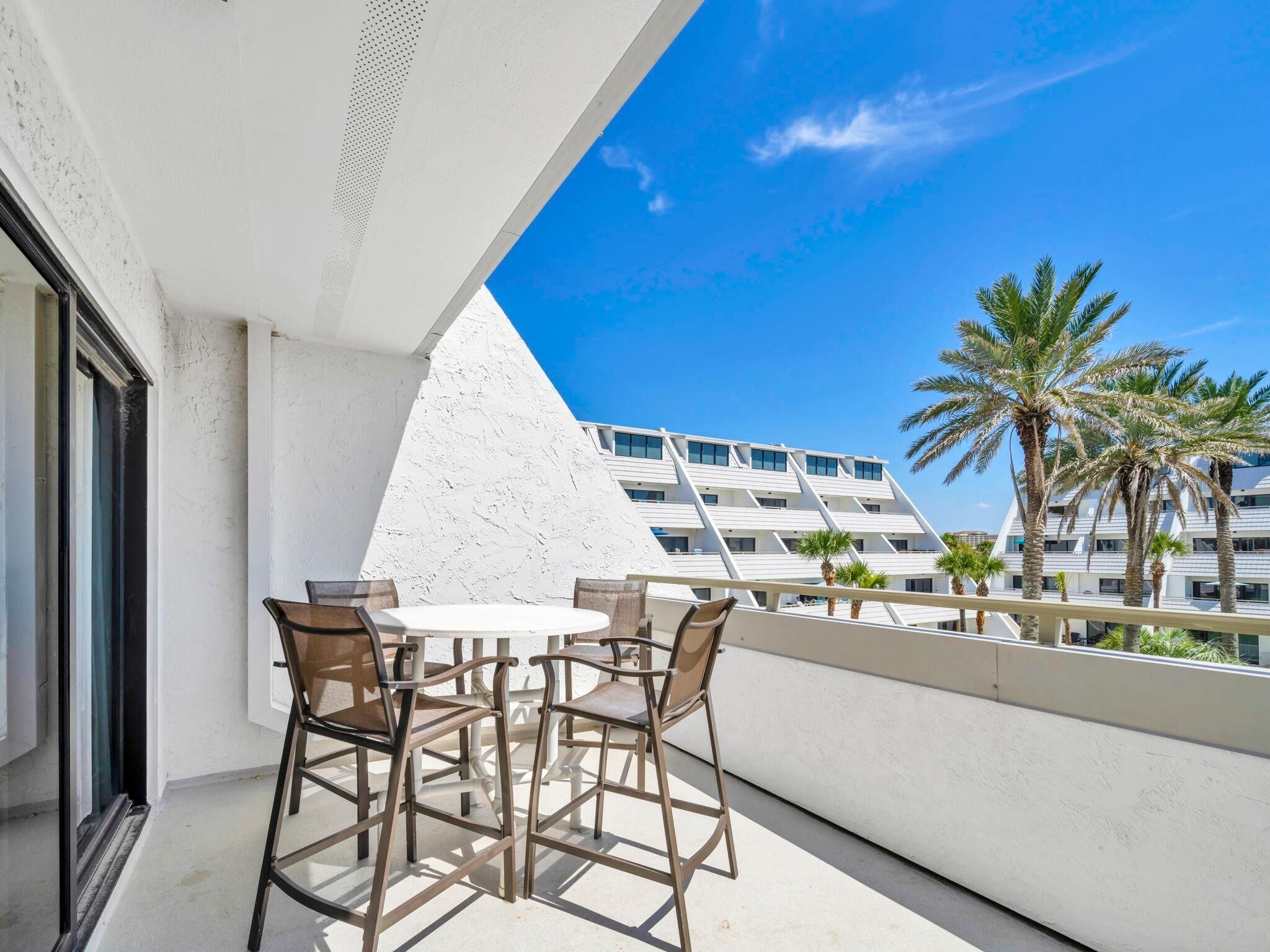 Un balcon avec une table et des chaises, donnant sur un immeuble moderne et des palmiers.