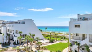 A modern hotel with a beach view, featuring multiple floors, outdoor seating, and palm trees. - Aegean 314 (Destin)