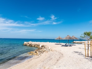 A beach with a rocky shoreline, clear blue water, and thatched umbrellas.