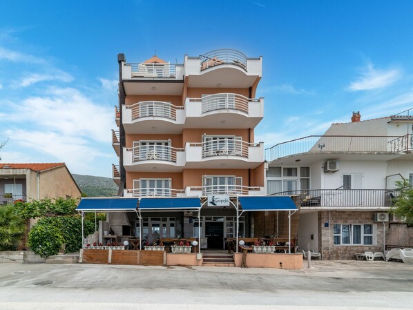 A multi-story hotel with a covered outdoor seating area and balconies on each floor.
