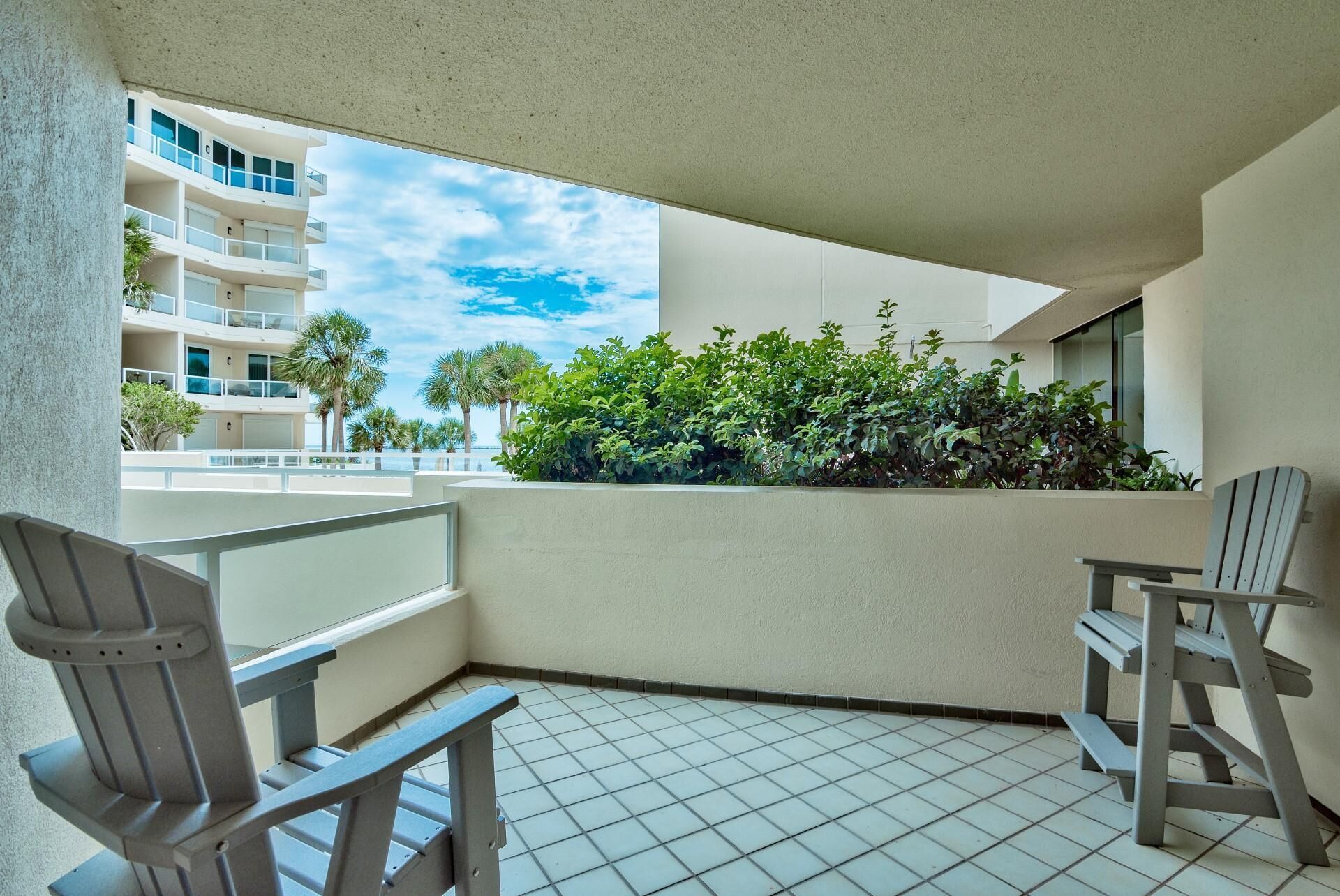 Un balcon avec deux chaises, un sol carrelé et une vue sur un immeuble doté de balcons et de palmiers.