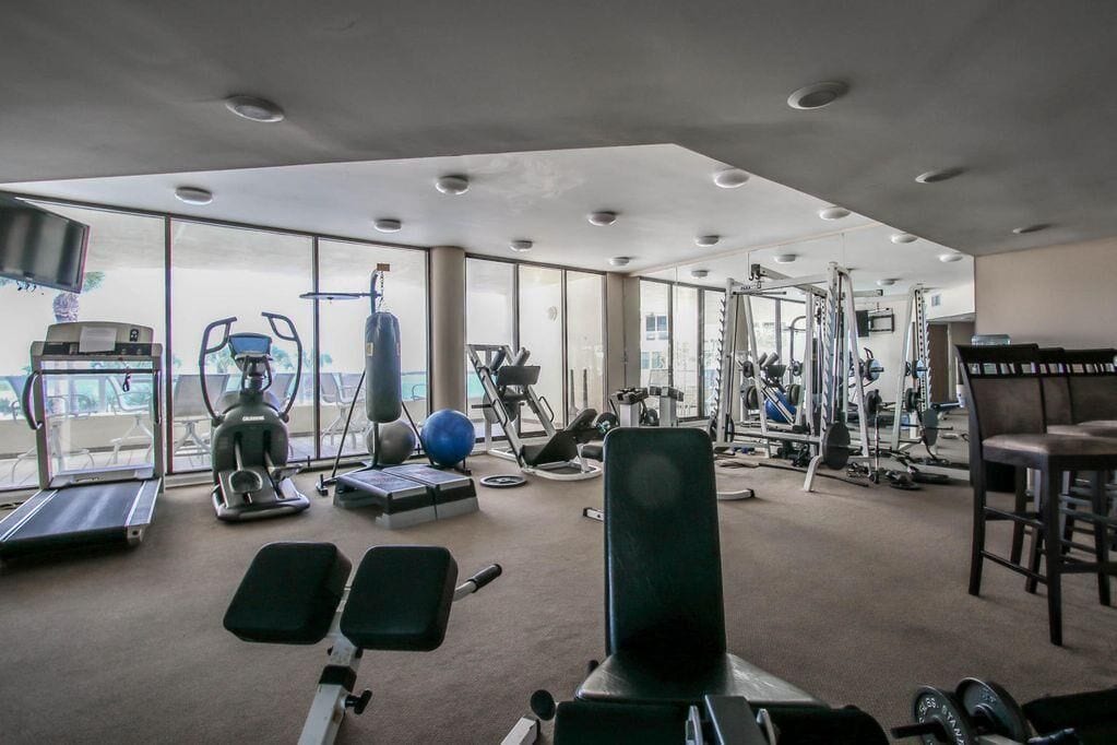 Un gimnasio con equipos de ejercicio variados, ventanas amplias y vistas al exterior.