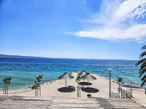 Ein Strand mit Reetdachschirmen, Liegestühlen und freiem Blick auf das Meer.