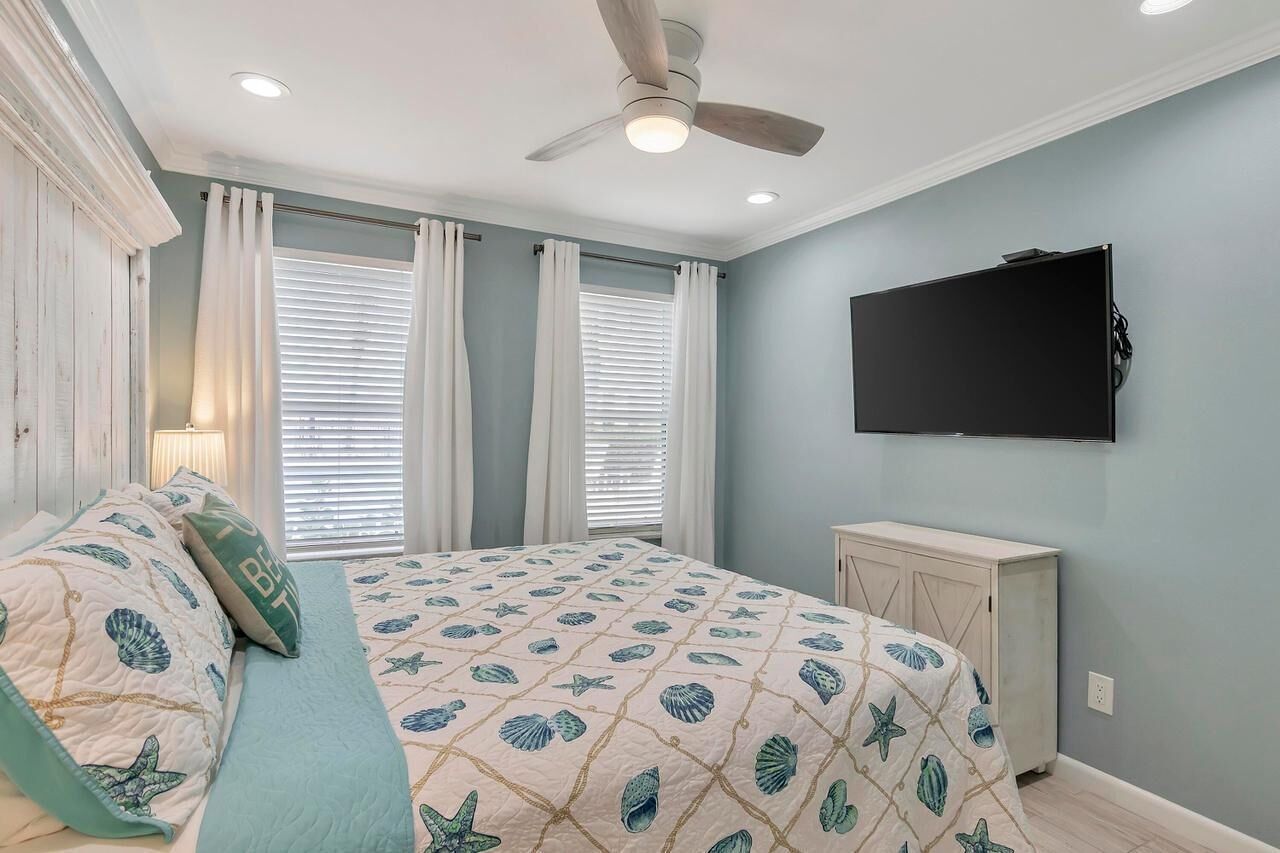 A bedroom with a bed, curtains, a ceiling fan, a TV, and a cabinet.