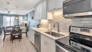 A modern kitchen with stainless steel appliances, a dining area with a round table and chairs, and light-colored cabinetry. - Poolside Villas 106 (Destin)