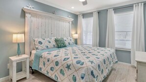 A bedroom with a bed, a nightstand, a ceiling fan, and a window with blinds. - Poolside Villas 106 (Destin)