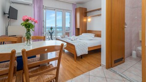 A hotel room with a bed, a dining table with chairs, a TV, a vase with flowers, and a view of the sea. - Jerkan 12 by Interhome (Podstrana)