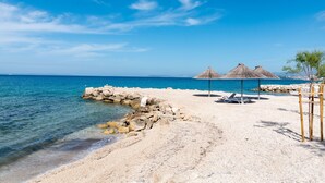 A beach with a rocky shoreline, clear blue water, and thatched umbrellas. - Jerkan 12 by Interhome (Podstrana)