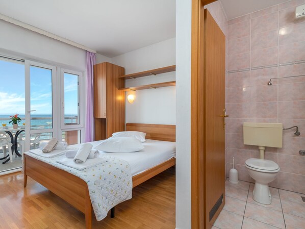 A hotel room with a wooden bed, a bathroom with a toilet and sink, and a balcony with a table and chairs.