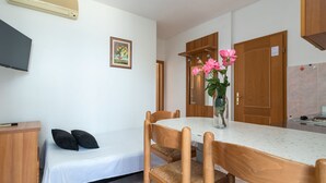 A small, clean room with a bed, a dining table with chairs, a wooden cabinet, a TV mounted on the wall, and a vase with flowers on the table. - Jerkan 11 by Interhome (Podstrana)