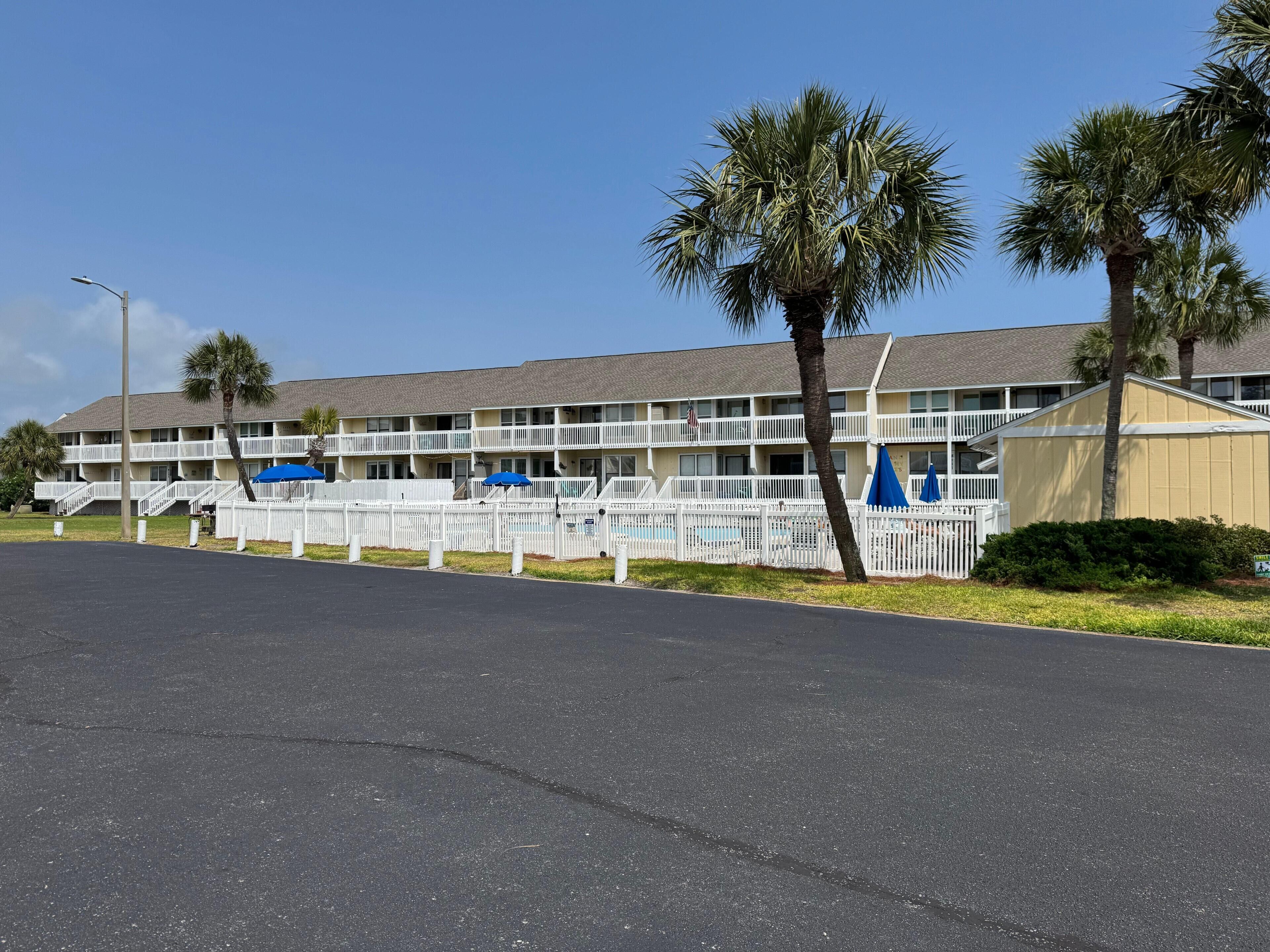 A motel with a pool, white fences, and palm trees.