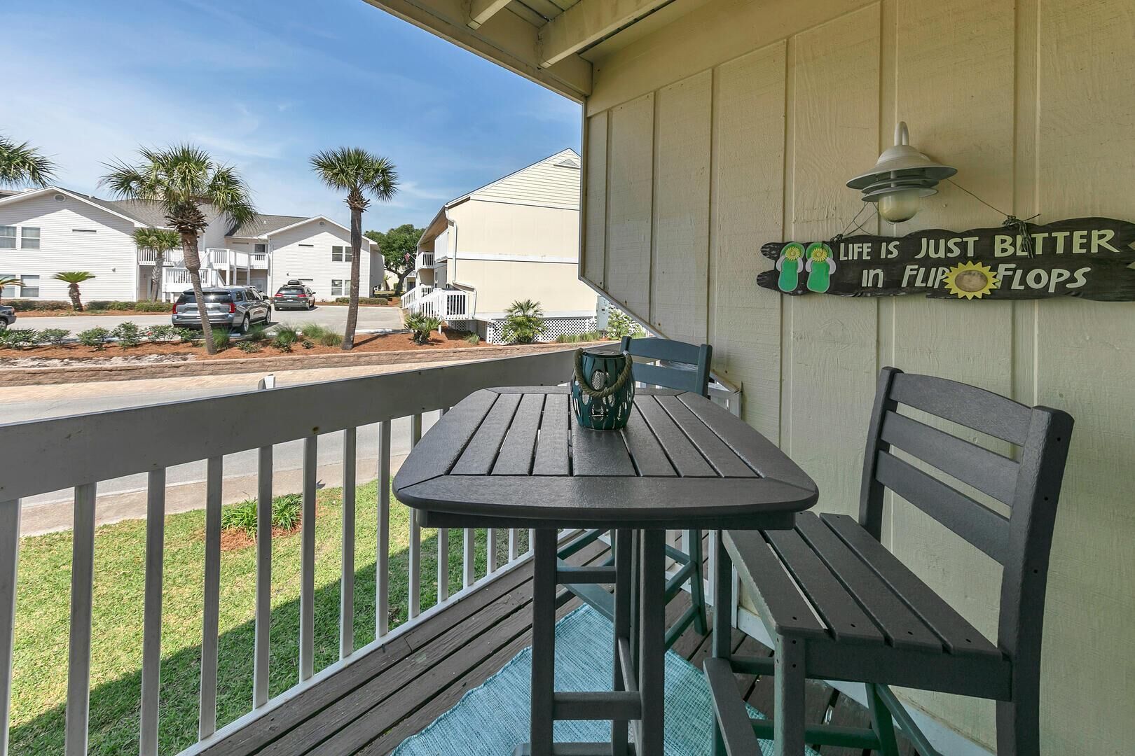 Un balcon avec une table et une chaise, une pancarte sur laquelle on peut lire « La vie est tout simplement plus belle en FLORIDE », et une vue sur une rue bordée de maisons et de palmiers.