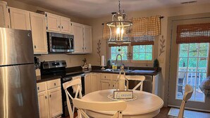 A kitchen with white cabinets, a stainless steel refrigerator, a microwave, and a dining area with a table and chairs. - Relax and enjoy this Country Charm! (Galena)