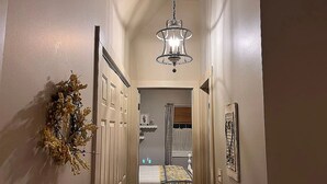 A narrow hallway with a bed in the background, a chandelier, and a wall-mounted decoration. - Relax and enjoy this Country Charm! (Galena)
