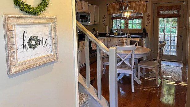 A kitchen with white cabinets, a dining table with chairs, a chandelier, and a window with blinds. - Relax and enjoy this Country Charm! (Galena)