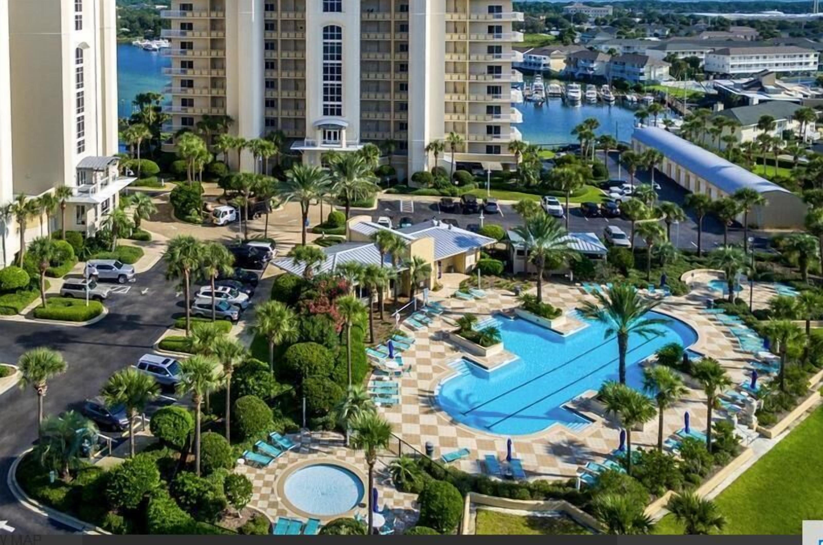 Un hôtel doté d’une grande piscine, de palmiers et offrant une vue sur l’eau.