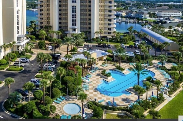 A hotel with a large pool, palm trees, and a view of the water. - Harbor Landing 203b (Destin)