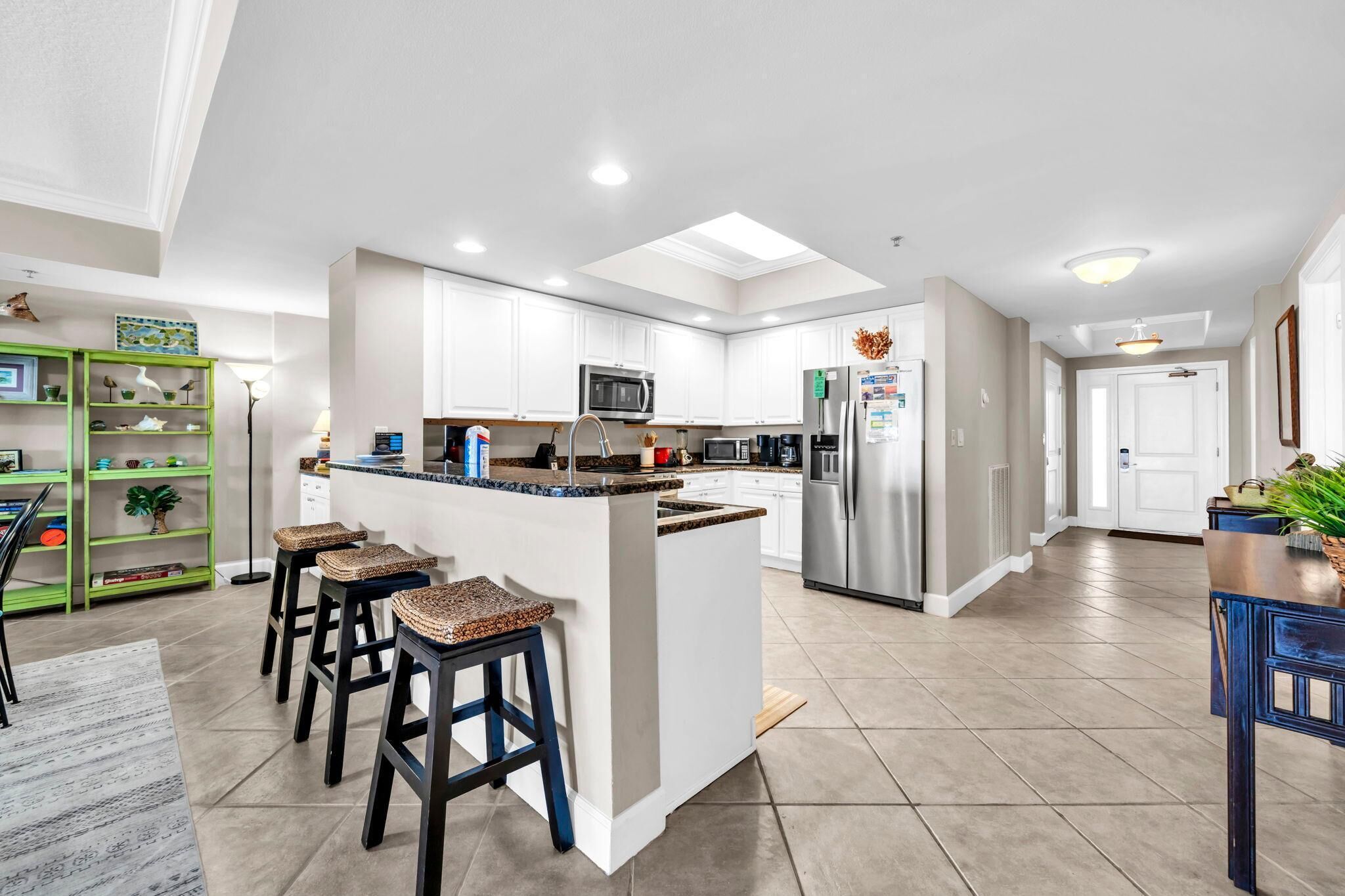 Una cocina moderna con armarios blancos, una isla central con taburetes, electrodomésticos de acero inoxidable y una estantería verde.