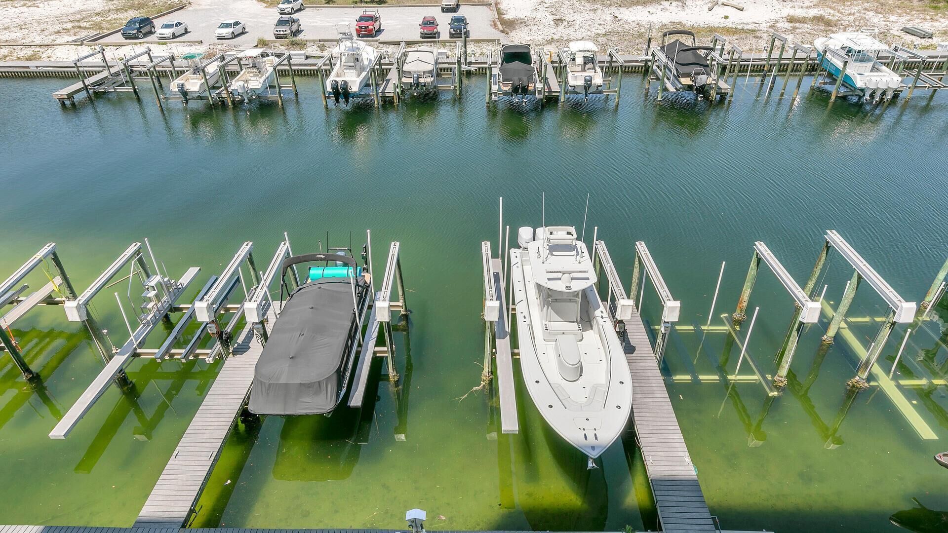 Een jachthaven met boten aangemeerd aan houten steigers, een overdekte aanhanger en een parkeerplaats met auto's.
