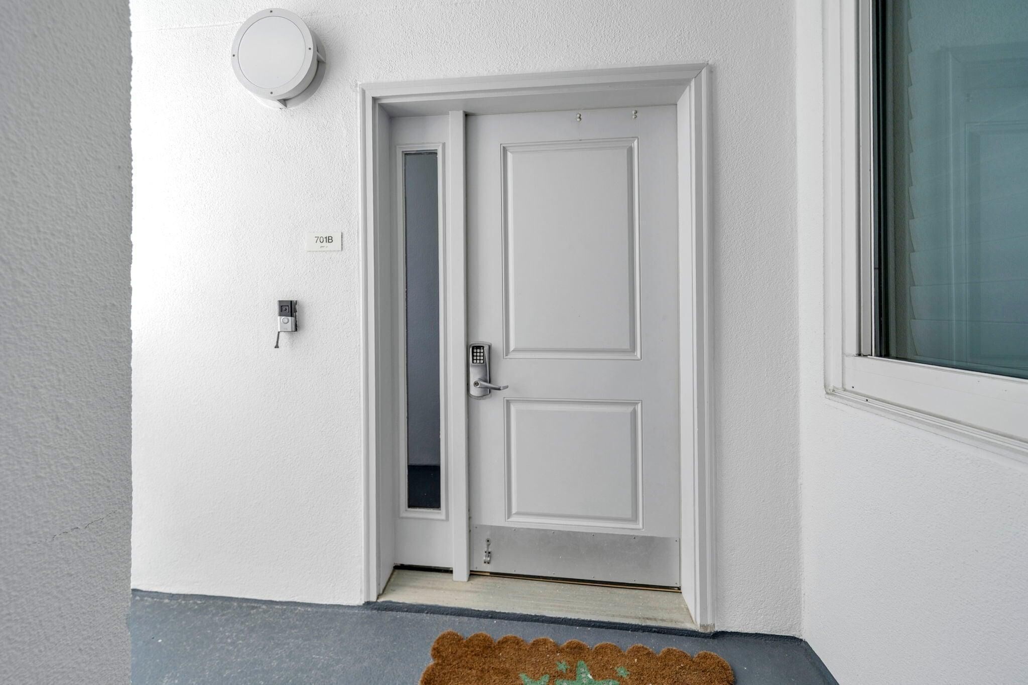 A white door with a keypad lock, a small window to the right, and a doorbell above it.