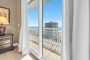 Una stanza con un'ampia porta scorrevole in vetro che dà su un balcone con vista sull'oceano e sugli edifici.