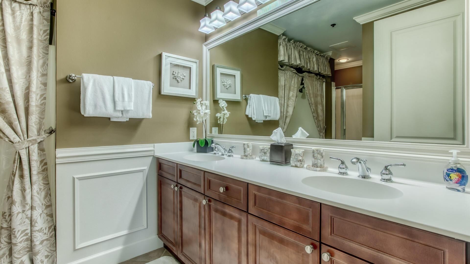 A bathroom with a double sink vanity, a large mirror, and two framed pictures on the wall.