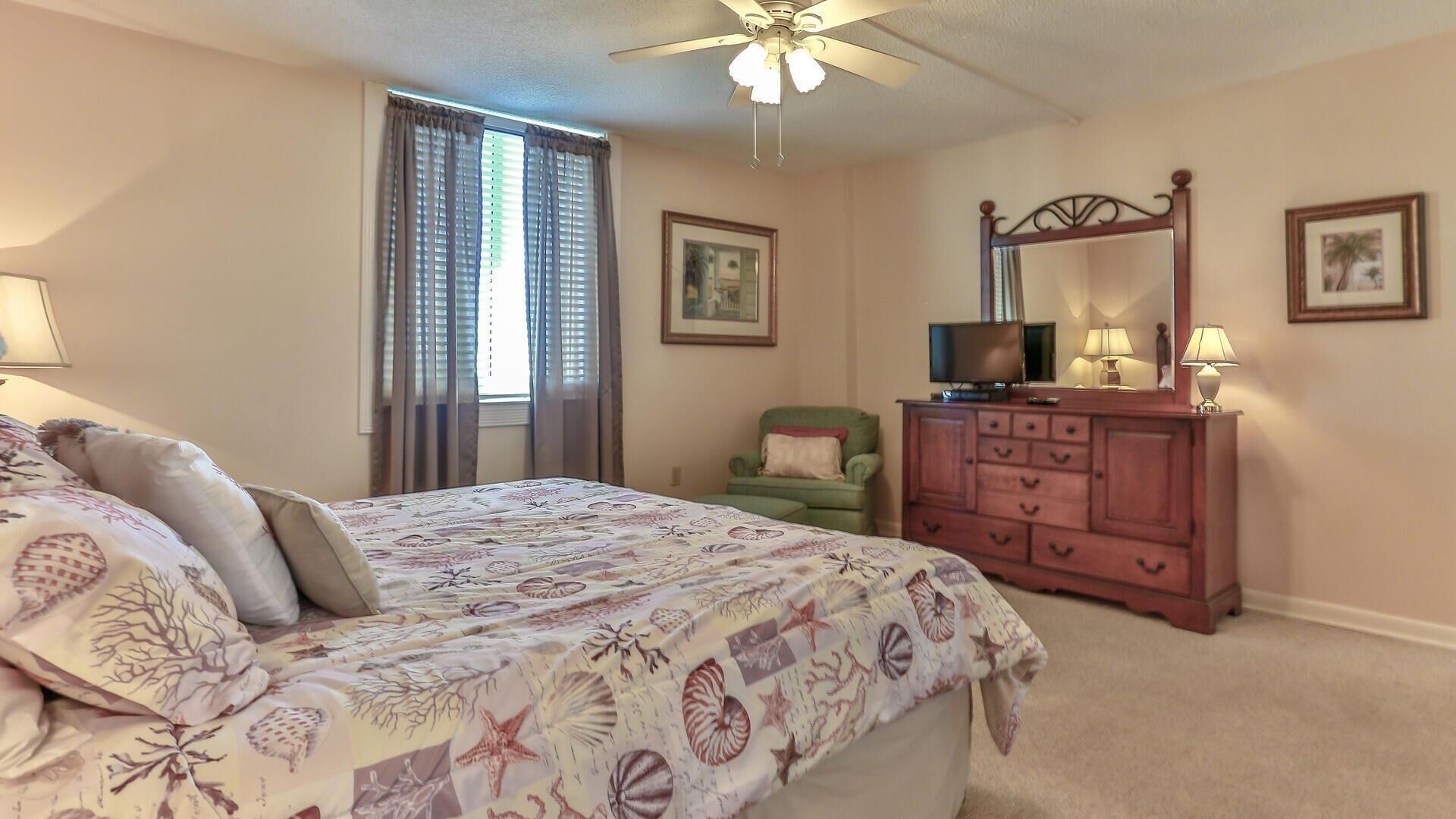 A bedroom with a bed, a dresser, a chair, a television, and a ceiling fan.