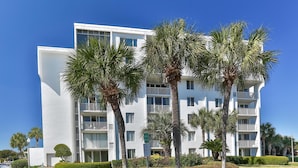Un hôtel à plusieurs étages doté de balcons, entouré de palmiers et de jardins bien entretenus.