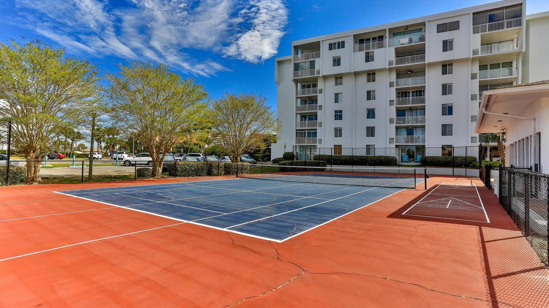 An outdoor tennis court with a multi-story building in the background.