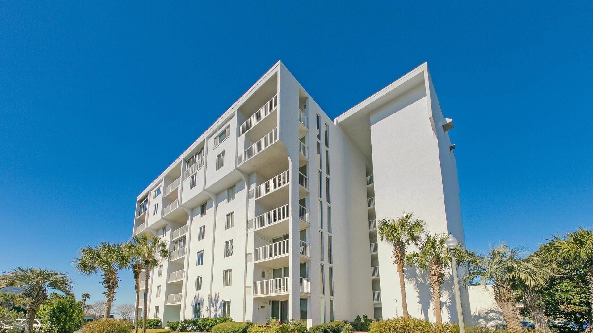 A multi-story hotel with balconies, a flat roof, and surrounded by palm trees.