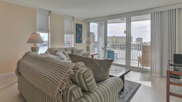 A spacious living room with a large sofa, a coffee table, and a view of the city through large windows. - Dolphin Point 402c (Destin)