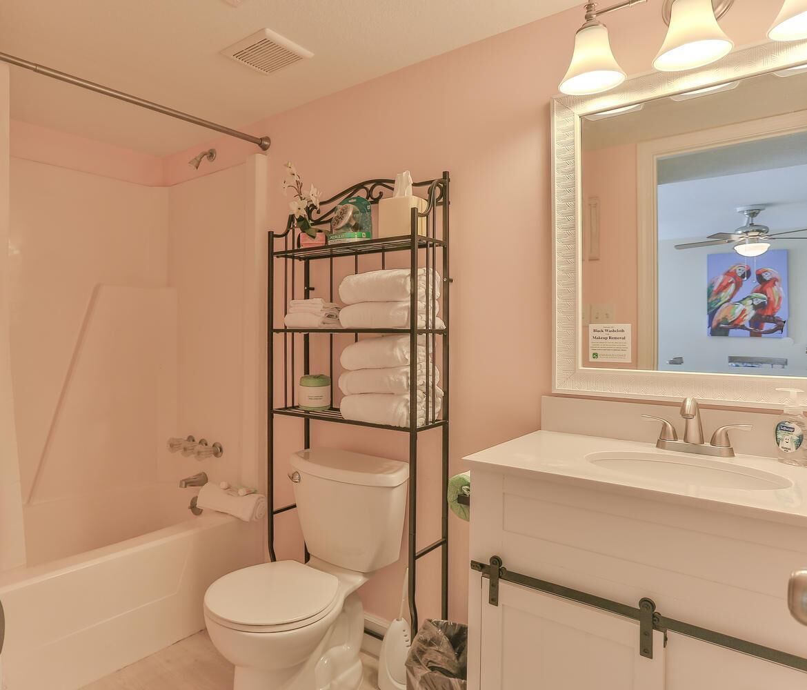 A bathroom with a white toilet, a shower, a vanity with a mirror, and a towel rack.