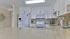 A modern kitchen with white cabinetry, a stainless steel refrigerator, a microwave, and a stove. - Dolphin Point 402c (Destin)