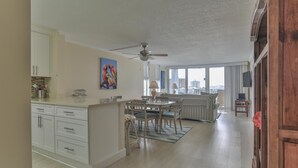 A spacious living area with a dining table, sofa, and a view of the city through large windows. - Dolphin Point 402c (Destin)